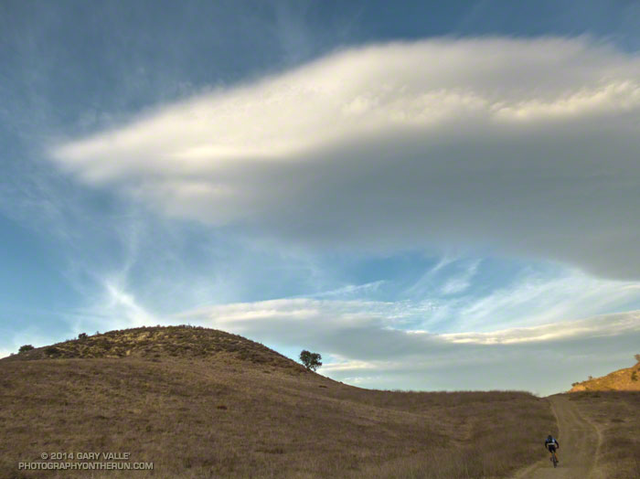 A mountain biker works up a hill with a huge wave cloud overhead.Higher frequency waves embedded in the primary wave.  Southern California, January 28, 2014.